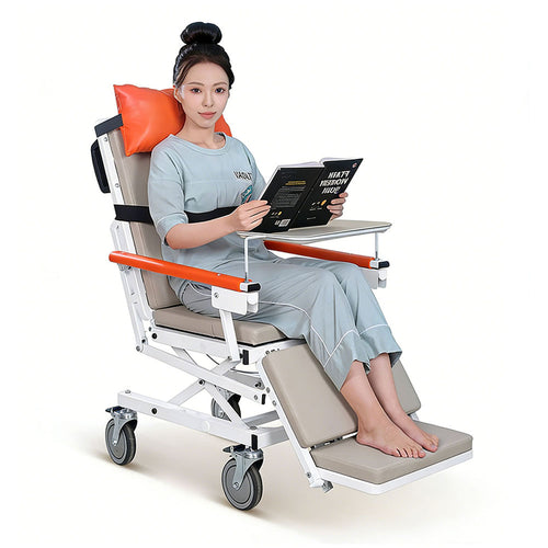 Woman reading a book while seated in the horizontal electric patient transfer chair with beige upholstery, orange head pillow and armrests, extended leg rest and swing-away tray table, on a white background